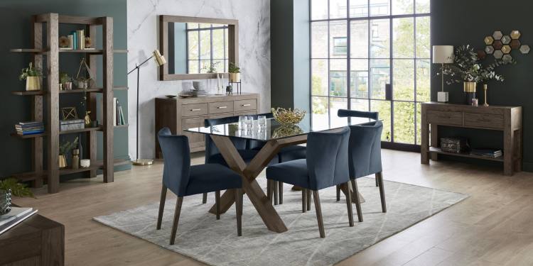 The Bentley Designs Turin Dark Oak Low Back Uph Chair in Dark Blue Velvet on Display with Dark Oak Table