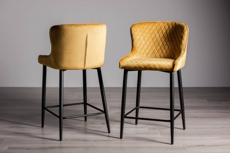 The Bentley Designs Cezanne Mustard Velvet Fabric Bar Stool with Sand Black Powder Coated Legs on Display